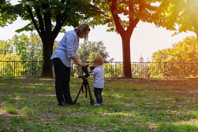 Full length of woman standing by tripod and son at park