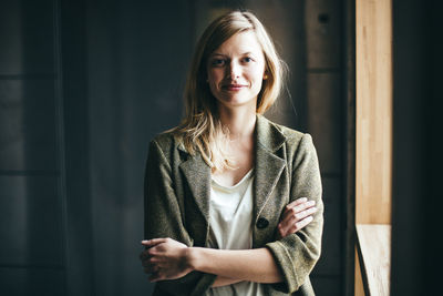 Portrait of smiling young woman standing against wall