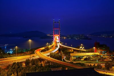 Light trails on road by illuminated city against sky at night