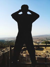 Rear view of silhouette man standing by railing against sky
