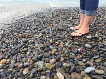 Low section of woman standing on pebbles at beach