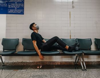 Side view of young man sitting on sofa against wall