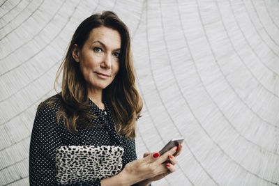 Portrait of businesswoman using mobile phone against wall at office