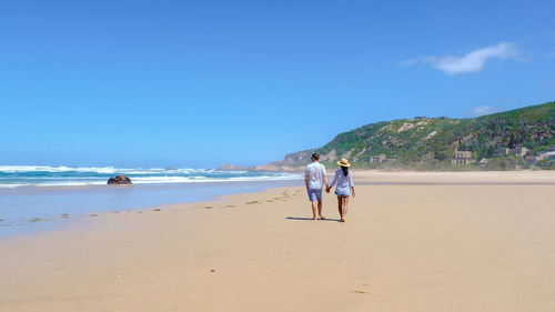 Rear view of woman walking at beach against clear blue sky