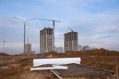 Construction site by modern buildings against sky