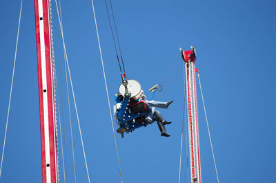 Low angle view of friends sitting on amusement park ride against clear blue sky