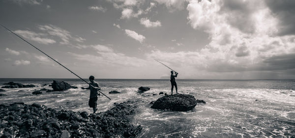 People fishing in sea against sky