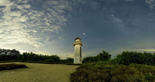 Lighthouse on field by building against sky at night