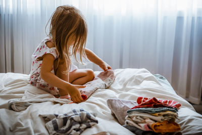 4 year old girl folding towels on a bed