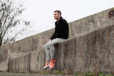 Side view of young man sitting against wall