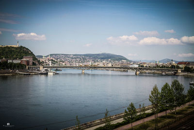 Bridge over river by buildings in city against sky