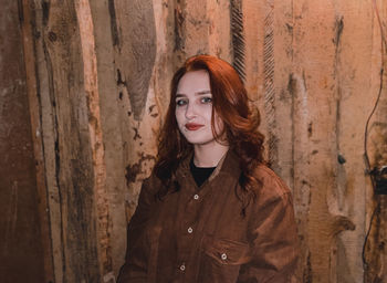 Portrait of beautiful young woman standing against wooden wall