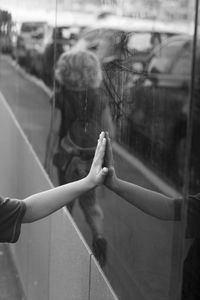 Cropped hand touching window with reflection of woman in city