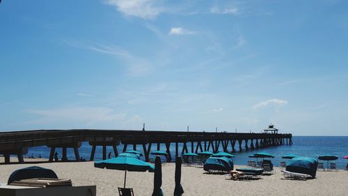 Pier on beach against blue sky