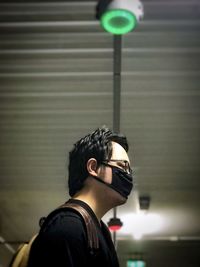 Low angle view of young man against illuminated ceiling and lights.