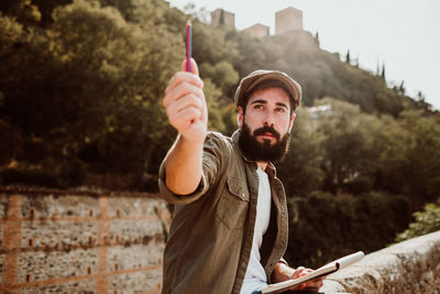 Man holding pencil and book while sitting outdoors