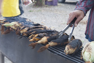 Cropped hand preparing corns on barbecue