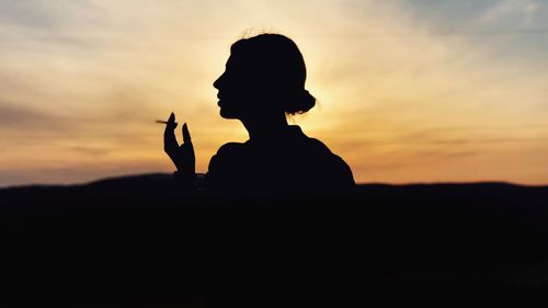 Silhouette man on rock against sky during sunset