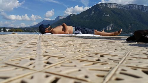 Surface level shot of shirtless man sleeping by lake against mountain