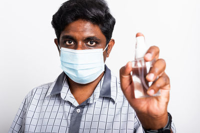 Portrait of man wearing mask holding sanitizer against white background