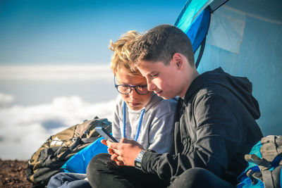 Brothers using mobile phone while camping on mountain