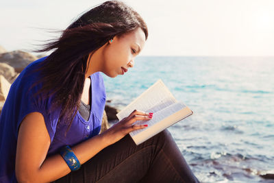 Young woman sitting on book at beach