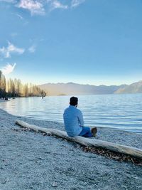 Rear view of man sitting on shore against sky