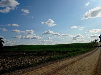 Road passing through field against cloudy sky