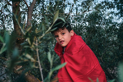 Child disguised as a red superhero rides a tree and makes a mean face