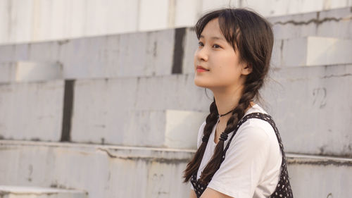 Side view of beautiful young woman looking away against wall