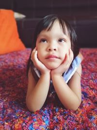 Portrait of cute baby girl sitting on bed at home