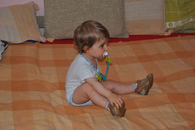 Cute baby boy sucking pacifier on bed at home