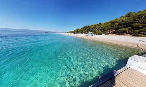 Swimming pool by sea against clear blue sky