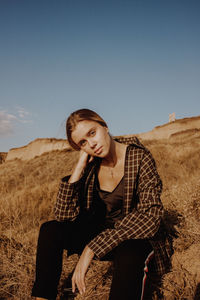 Full length of young woman sitting on field against clear sky