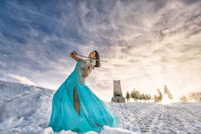 Woman playing on violin against sky during sunset