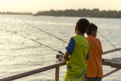 Rear view of boys on pier fishing in river