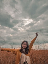 Portrait of smiling young woman standing on field against sky