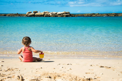 Girl sitting on beach against sky