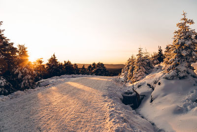 Snow covered field against sky during sunset
