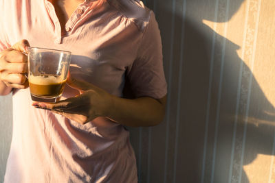 Midsection of woman having coffee against wall