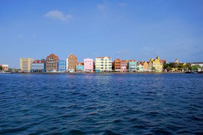 Sea by buildings against blue sky