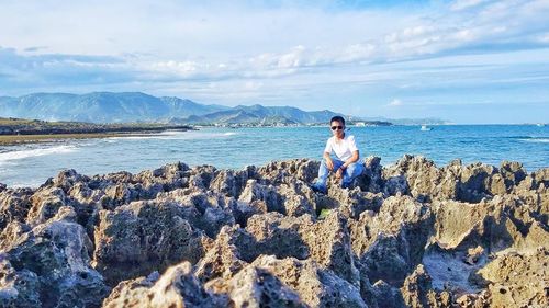 Woman standing on rock by sea against sky