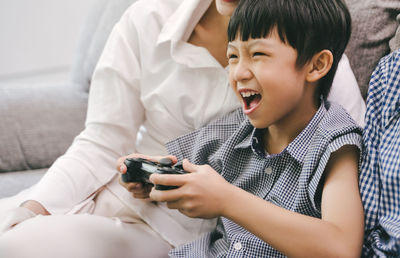 Mother and daughter holding camera while sitting on sofa