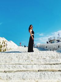 Full length of woman standing on steps against blue sky