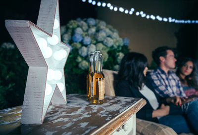 Star shape lighting equipment by beer bottles on table with friends in background at night