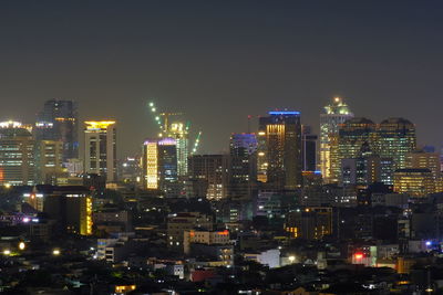 Illuminated modern buildings in city against sky at night