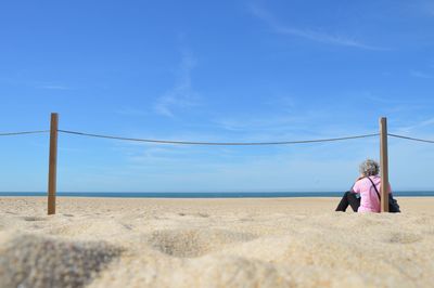 Rear view of couple walking on shore against blue sky