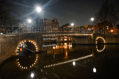 Illuminated bridge over river in city at night