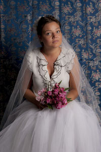 Portrait of woman with pink flower standing against wall