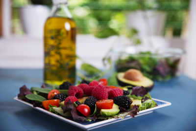Salad with red berries, cherry tomatoes and avocado, on a blue table.